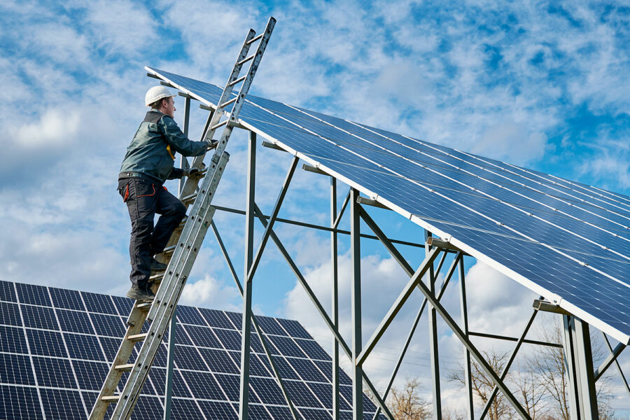 Un operario sube una escalera mientras instala placas solares